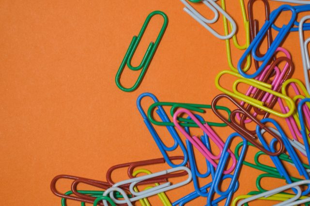 A pile of colorful paper clips on an orange background.