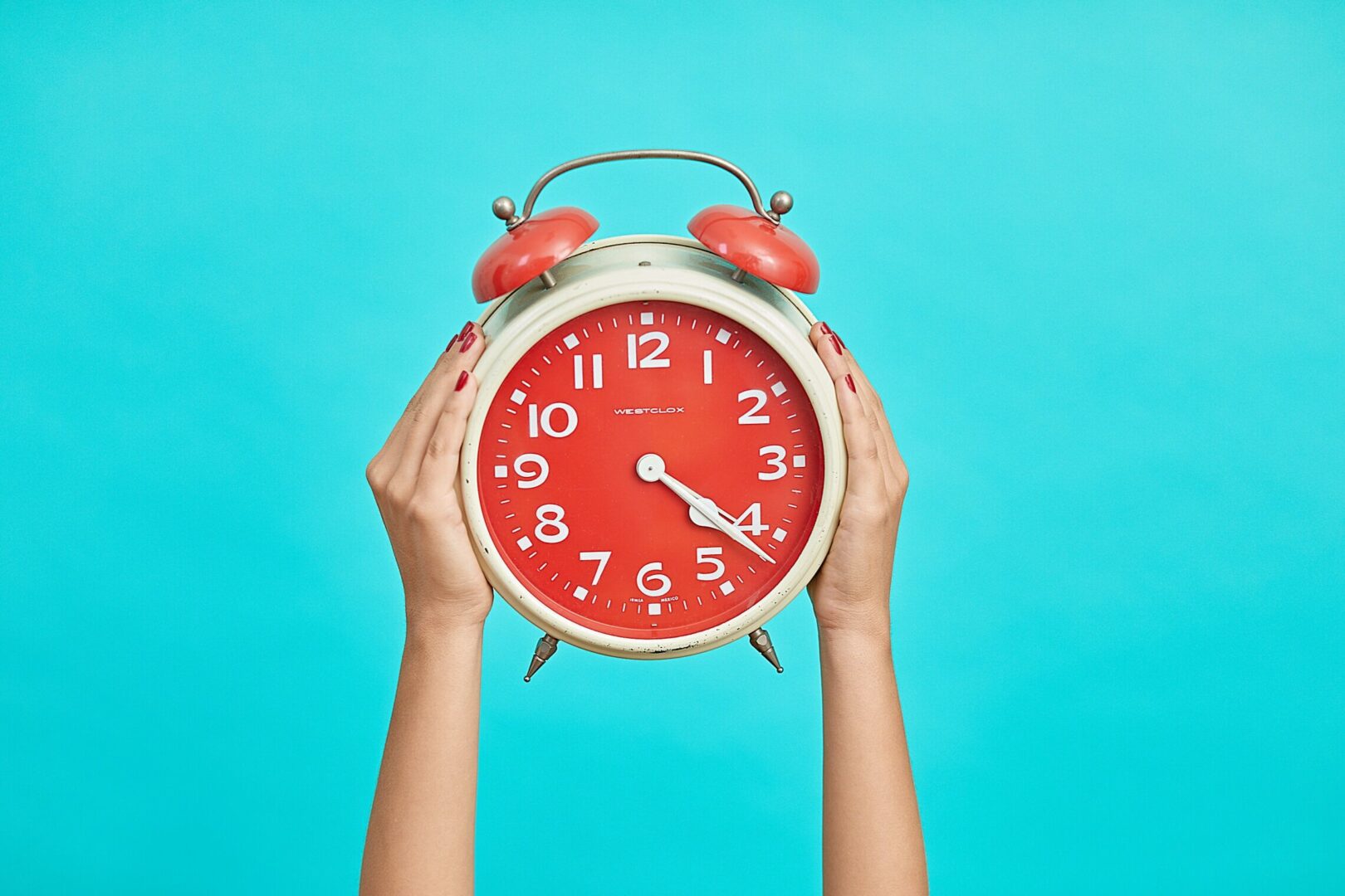 A woman's hands are holding up an alarm clock on a blue background.