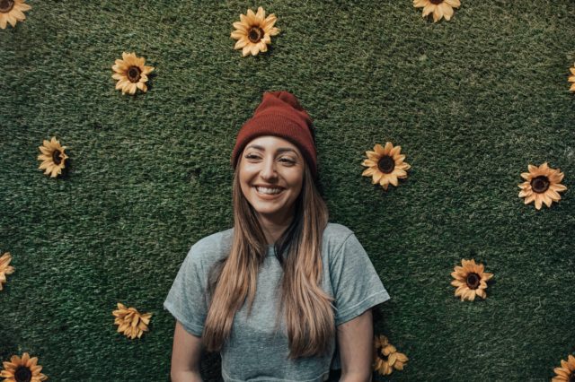 A young woman smiling in front of a wall of sunflowers.