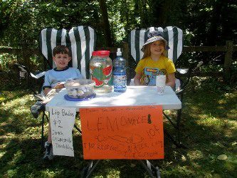 Two children sitting at a table with a sign on it.