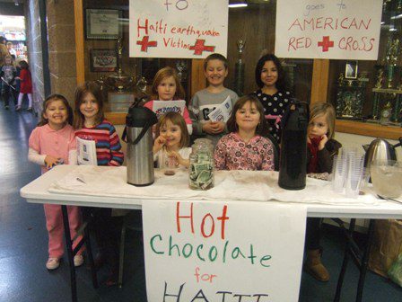 A group of children standing in front of a table with a sign that says hot chocolate for haiti.
