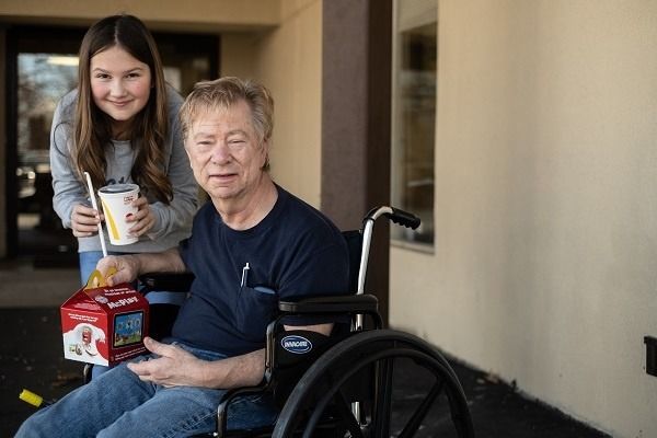 A man in a wheelchair with a girl holding a cup of coffee.