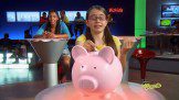 A girl sitting at a table with a pink piggy bank.