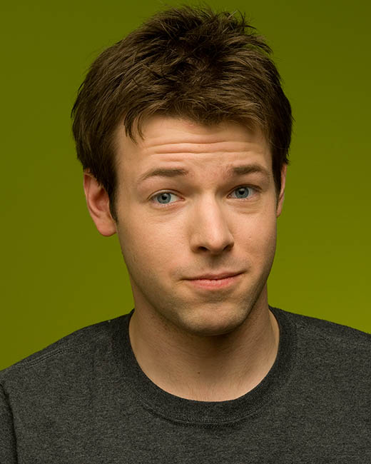 A young man in a gray shirt is looking at a green background.