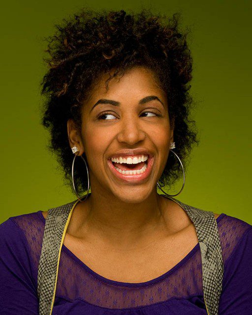 A woman laughing with a purple shirt and hoop earrings.