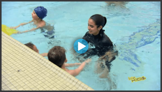 A woman in a wetsuit is playing with children in a swimming pool.
