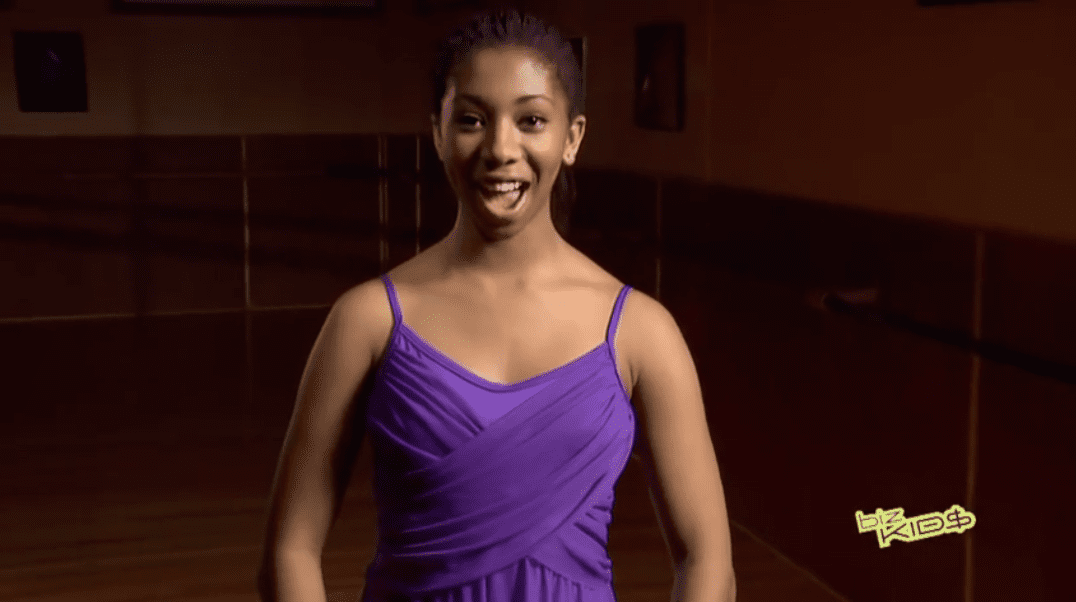 A girl in a purple dress is smiling in a dance studio.