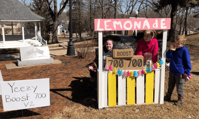 A lemonade stand with children in front of it.