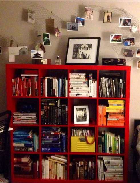A red bookcase in a bedroom with books on it.