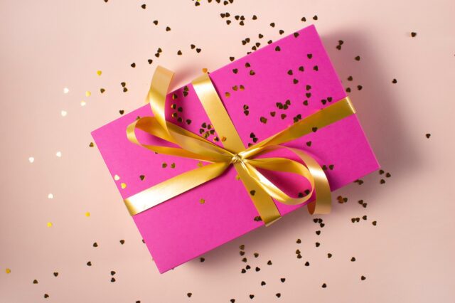 A pink gift box with gold confetti on a pink background.