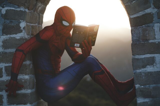 Spider - man reading a book out of a window.