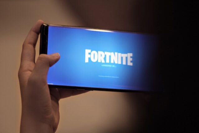A person is holding up a phone with the fortnite logo on it.