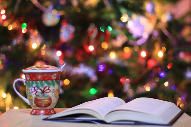 A cup of coffee and a book on a table in front of a christmas tree.