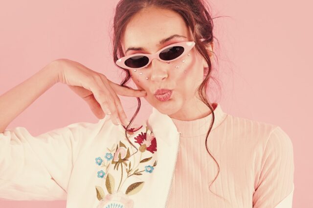 A woman wearing sunglasses on a pink background.