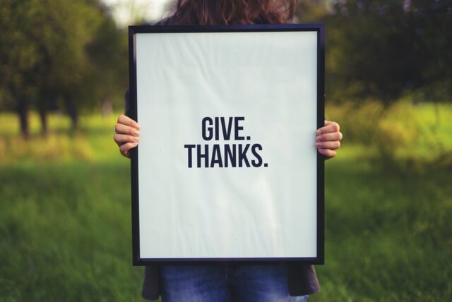 A woman holding up a sign that says give thanks.