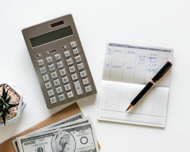A calculator, pen and money on a white table.
