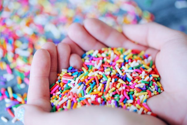 A person's hands holding a pile of colorful sprinkles.