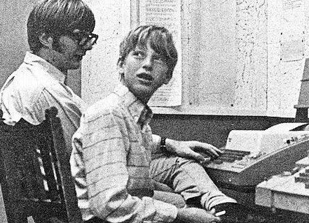 Two men sitting at a desk with a computer in front of them.