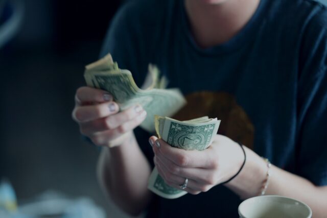 A woman is holding money in front of a coffee cup.
